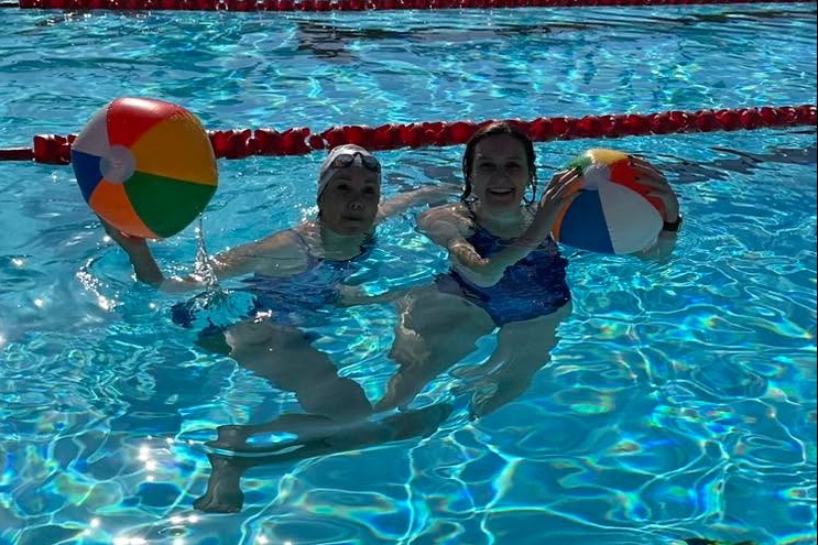 Two swimmers in the pool, each holding a colourful beach ball.