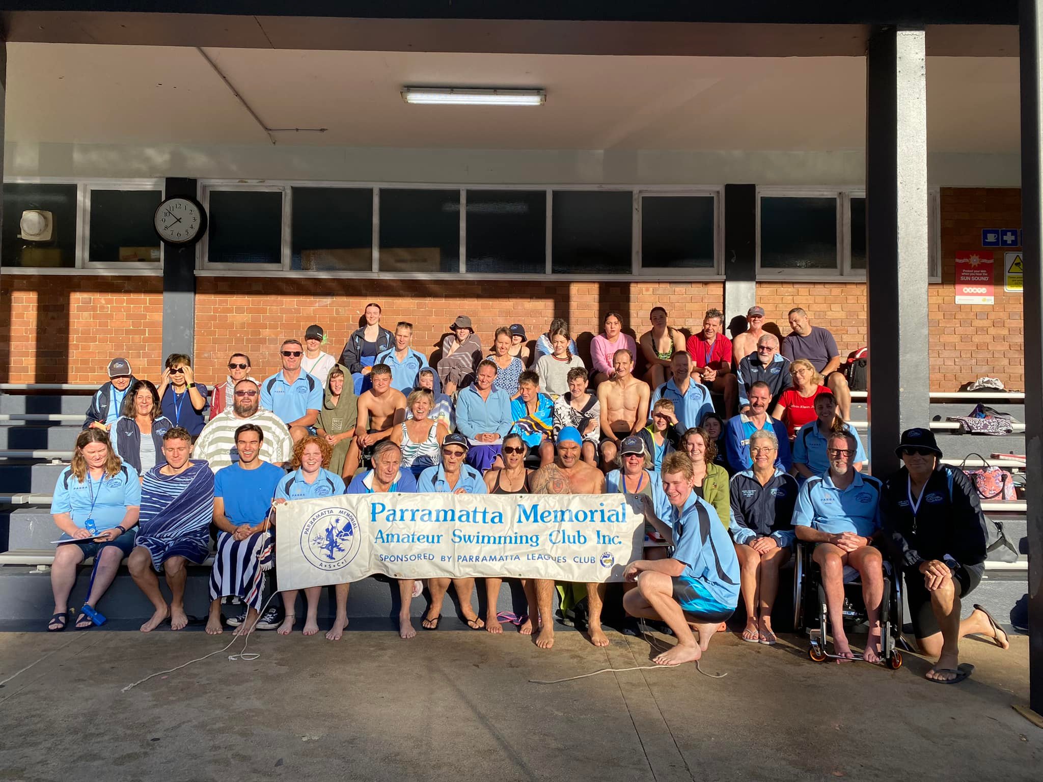 Club members seated and standing beneath the grandstand shelter at Epping with the Club banner.