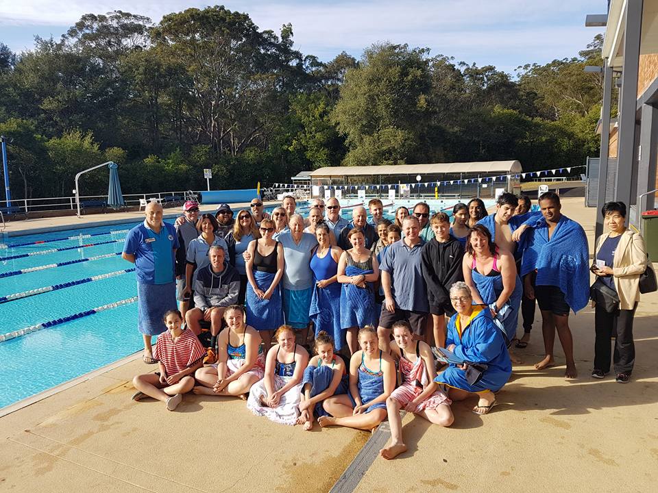 A large group of Club members in Club shirts on the pool deck at Epping, with bushland behind the pool.