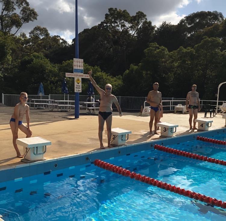 Four swimmers of different ages on the starting blocks at Epping Aquatic Centre, the oldest with one arm raised.