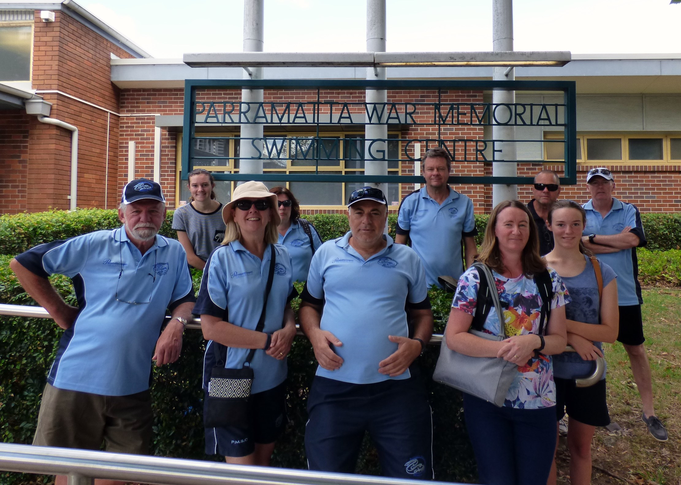 Club members in Club shirts standing in front of the Parramatta War Memorial Swimming Centre sign at the pool entrance.