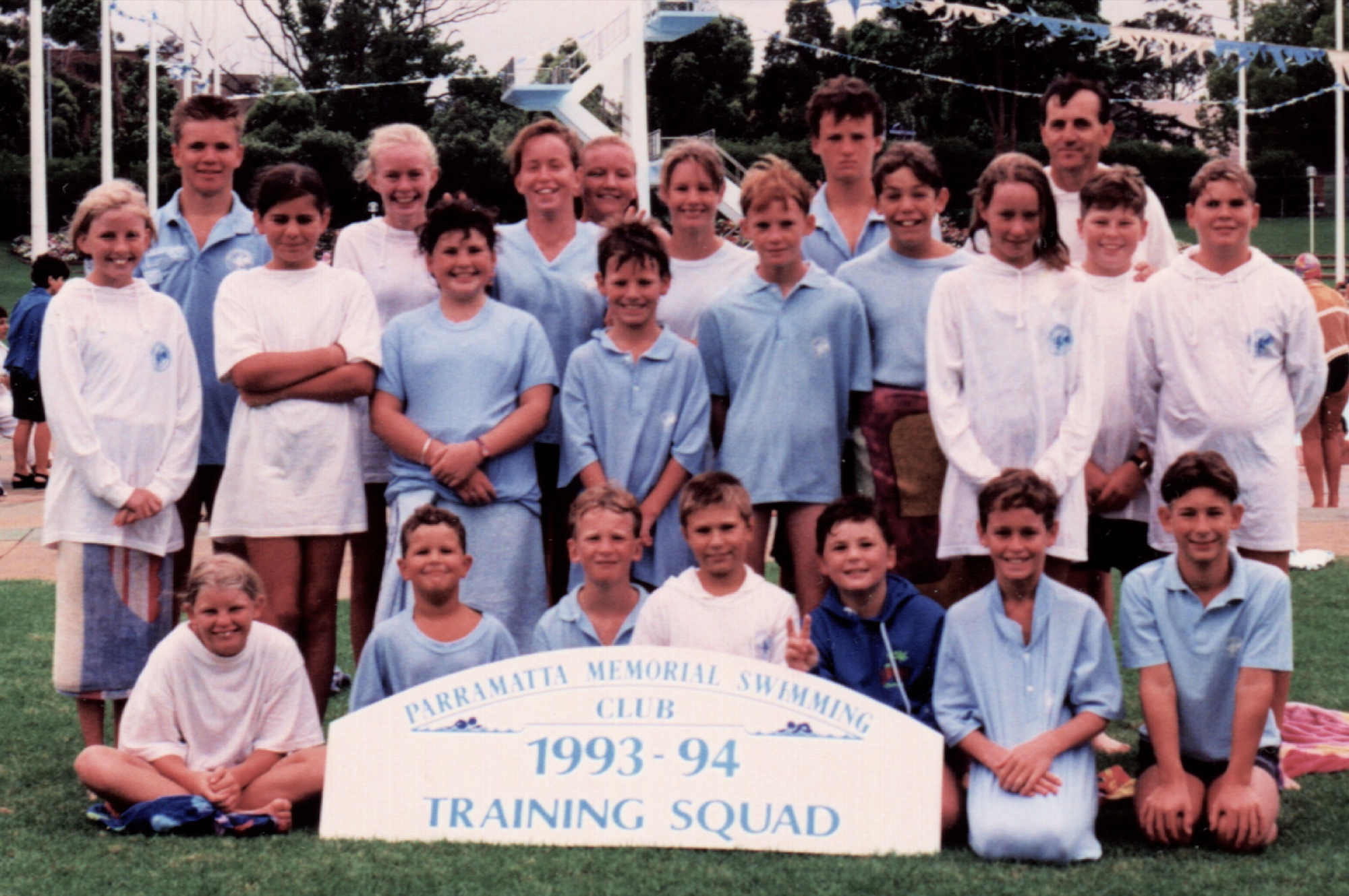 Around 30 young swimmers and coaches on the grass at the old Parramatta pool behind a “1993–94 Training Squad” sign.